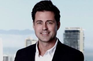 A smiling man in a blazer poses confidently against a modern city backdrop, showcasing a professional and polished appearance.