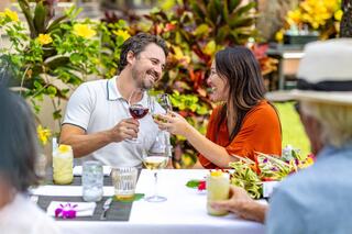 A couple shares a joyful toast at an outdoor table adorned with vibrant flowers and drinks, surrounded by a cheerful atmosphere.