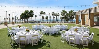 A modern beachfront hotel overlooks the ocean, surrounded by palm trees and beach access, under a clear sky.