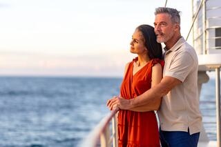 A couple stands together by the railing, gazing thoughtfully at the sea as the sun sets, highlighting their connection and serene atmosphere.