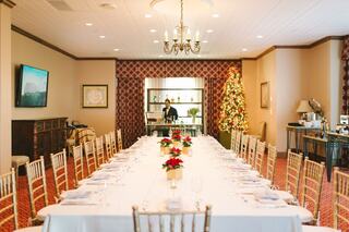 A long dining table is elegantly set with floral centerpieces, surrounded by golden chairs, and a festive Christmas tree in the background.