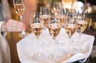 A tray holds several elegant champagne flutes filled with bubbly, while a hand reaches for one. The setting exudes celebration and sophistication.