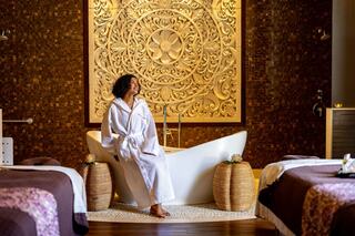 A woman in a white robe relaxes in a luxurious spa setting, featuring intricately designed walls and a serene atmosphere.