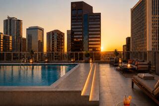 A serene rooftop pool overlooks a city skyline at sunset, with cozy seating and drinks, creating a perfect tranquil escape.