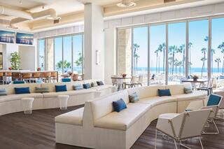 Bright, modern lounge with large windows showcasing palm trees and ocean views, featuring curved seating and inviting decor.