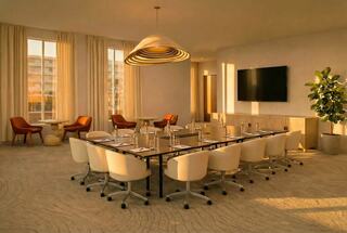 A modern conference room with a long table, ergonomic chairs, warm lighting, and large windows, creating a welcoming atmosphere.