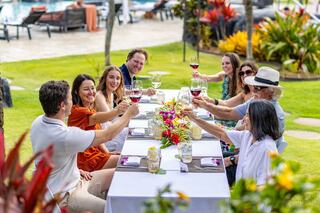 A cheerful group of friends raises their glasses in a toast at a beautifully arranged outdoor table, surrounded by vibrant flowers and greenery.