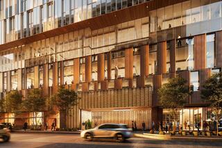A modern building features large glass panels and wooden accents, with greenery at the base and pedestrians walking along a bustling street.