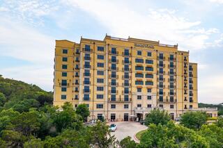 A tall, yellow hotel building nestled among lush greenery, featuring multiple balconies and a welcoming entrance.