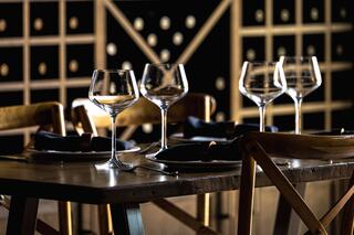 A cozy dining table set with elegant wine glasses and dark napkins, complemented by a backdrop of wine racks, creating an inviting atmosphere.