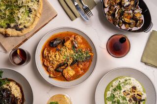A curated spread of delicious seafood pasta, mussels, grilled dishes, and drinks elegantly arranged on a marble table.