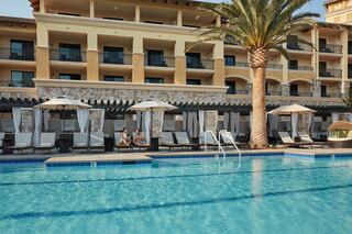A tranquil resort scene featuring a sparkling pool, cozy cabanas, and a palm tree, with guests relaxing nearby under sunny skies.