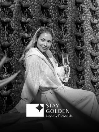 A woman in a robe holds a glass of champagne, seated against a textured wall, radiating luxury and relaxation.