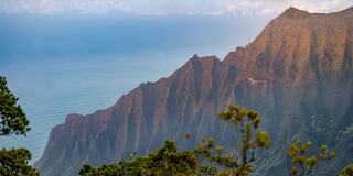 Stunning cliffs rise dramatically above a calm ocean, with lush greenery framing the scene under a soft, cloudy sky.