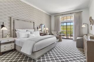 A spacious, elegantly designed hotel room featuring a large bed, stylish furnishings, and a view through expansive windows.