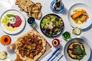 A vibrant spread featuring gourmet dishes, including salad, salmon, a savory pizza, and drinks, all beautifully arranged on a table.