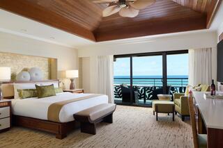 A stylish hotel room features a king-size bed, modern décor, and a balcony overlooking the ocean, complemented by warm wooden accents.