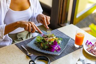 A person enjoys a vibrant salad garnished with an orchid, accompanied by a glass of juice and coffee on a stylish table.