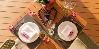 A beautifully set table awaits a romantic dinner, adorned with flowers, elegant dinnerware, and a heart-shaped arrangement.