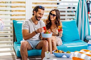 A couple enjoys a vibrant summer day on a cozy couch, sharing food and drinks, radiating joy and relaxation.