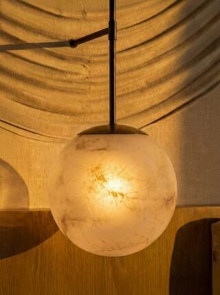 A warm, glowing spherical pendant light with subtle marbling hangs against a textured backdrop, adding elegance to the space.