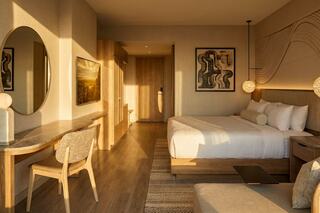 A modern hotel room featuring a stylish bed, wooden accents, cozy seating, and warm lighting, creating a welcoming and serene atmosphere.