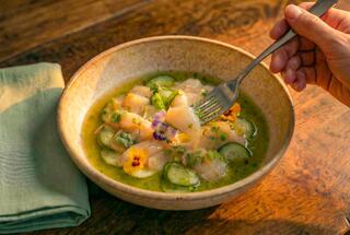 A bowl of fresh seafood garnished with herbs and edible flowers, accompanied by a fork and a green napkin on a wooden table.