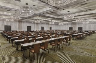 A spacious conference room features rows of tables and chairs, elegantly lit by chandeliers, with a modern, patterned carpet.