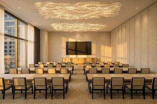 A modern conference room featuring rows of tables and chairs, large windows, and an elegant ceiling design illuminated by soft lighting.