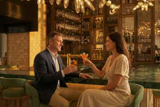 A couple enjoys drinks at a stylish bar, engaging in conversation with smiles, amidst warm lighting and an inviting atmosphere.
