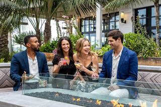 A group of four friends enjoys cocktails by a firepit in a stylish outdoor setting, surrounded by greenery and vibrant decor.