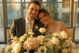 A happy couple smiles warmly together at a wedding, surrounded by a beautiful floral arrangement, radiating love and joy.