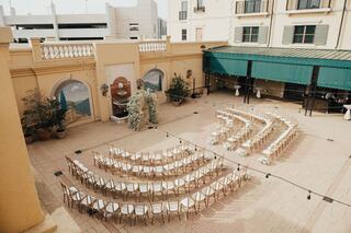 A charming outdoor venue with elegant rows of chairs, decorated greenery, and string lights, ideal for a wedding ceremony.