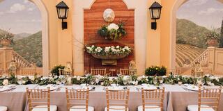 A beautifully arranged table is set with elegant dinnerware, surrounded by floral decorations and a scenic mural backdrop.