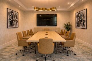 A modern conference room features a long wooden table, ergonomic chairs, a wall-mounted TV, and stylish artwork, creating a professional atmosphere.