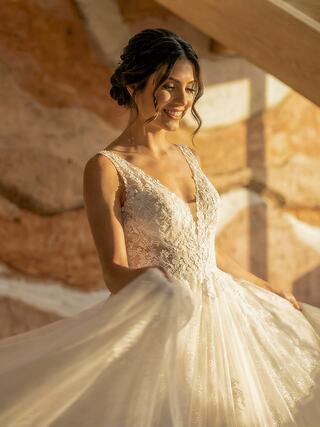 A smiling bride in a stunning lace gown twirls in warm light, surrounded by natural textures, radiating joy and elegance.