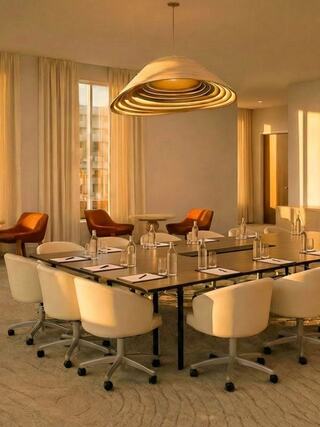 A stylish conference room features a large table surrounded by modern chairs and warm lighting, creating a professional yet inviting atmosphere.