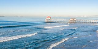 A serene coastal scene with gentle waves lapping at a wooden pier, under a clear blue sky and distant land on the horizon.