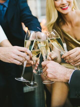 Glasses of champagne are raised in celebration amid a gathering of friends, with smiles and an elegant atmosphere.