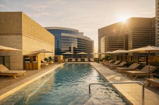 A serene rooftop pool surrounded by modern architecture, lounge chairs, and umbrellas, bathed in warm sunlight.