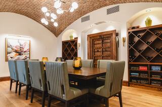 A stylish dining room featuring a wooden table, plush chairs, wine racks, and an arched ceiling, illuminated by modern lighting.