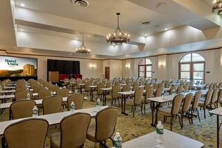 A well-lit conference room features rows of tables and chairs, with a stage and screen at the front, ready for an event.