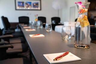 A sleek conference room features a long table set with pens, notepads, and glasses, accented by a floral water pitcher.