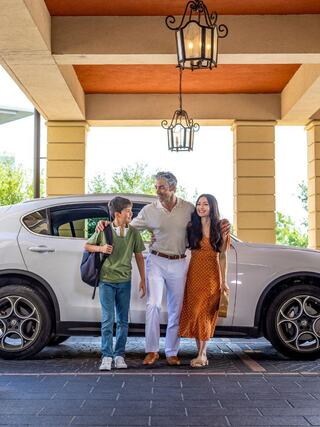 A happy family stands together outside a stylish car, enjoying a sunny day, with a warm and inviting atmosphere around them.