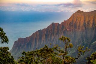 Dramatic cliffs rise steeply from the ocean, cloaked in lush greenery under a soft, pastel sky, creating a breathtaking coastal landscape.